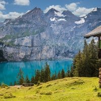 a photo of a cabin on a lake in switzerland with the mountains in the background.