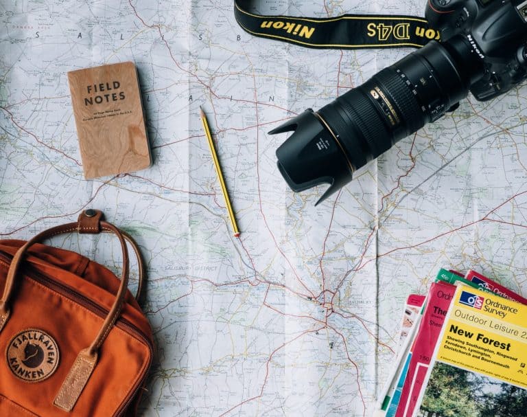 overhead view of bag, pencil, notepad, camera, and books on top of a map