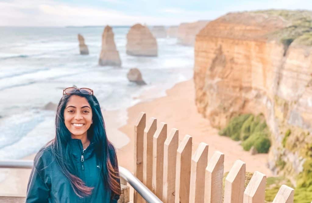 A photo of me in a jacket posing in front of the 12 Apostles which are the most iconic Great Ocean Road stops.