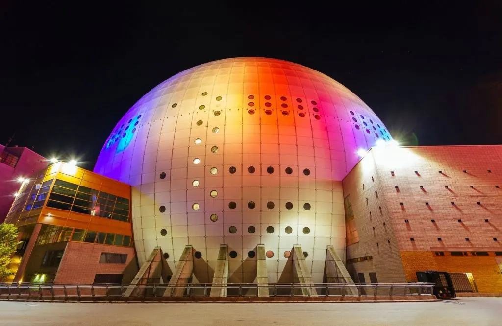 A colorful dome at night that's lit up and is known as the Avicii Arena