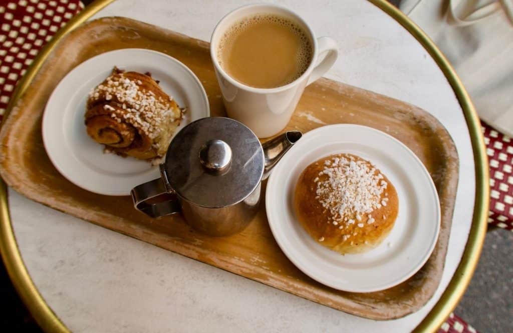 A tray on a table with coffee and two pastries that are topped with nuts and powdered sugar