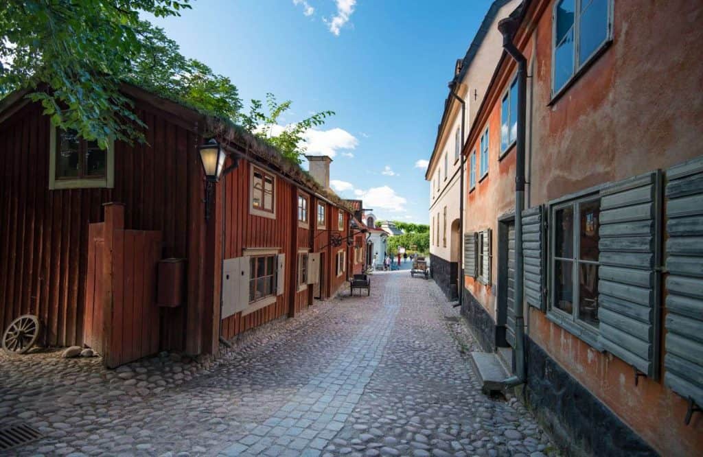 Cobblestone street with older buildings on both sides of the street making up Skansen open air museum