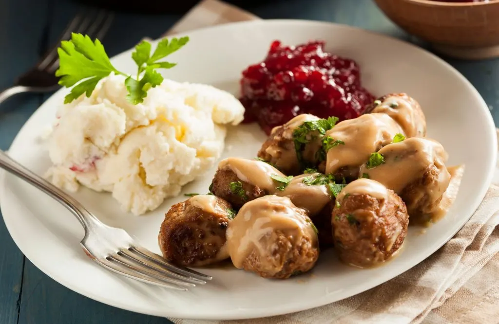 A plate with Swedish meatballs, mashed potatoes, and a red sauce