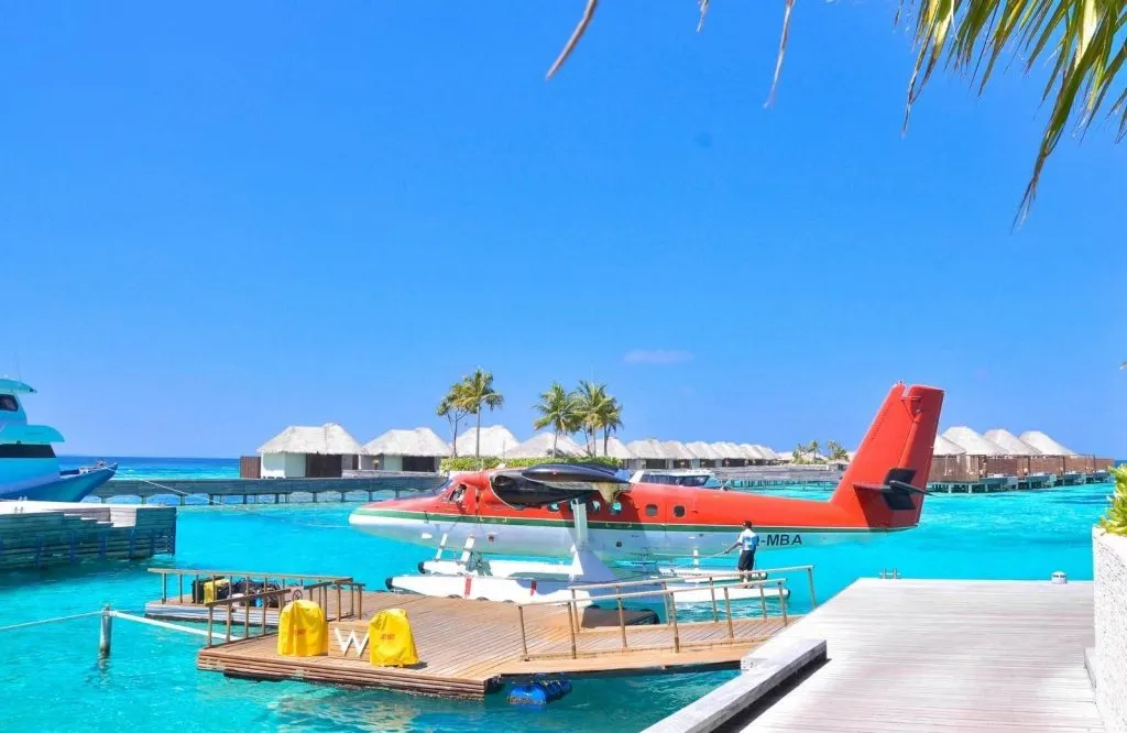 A red seaplane on a jetty with clear blue skies and a deep blue ocean.