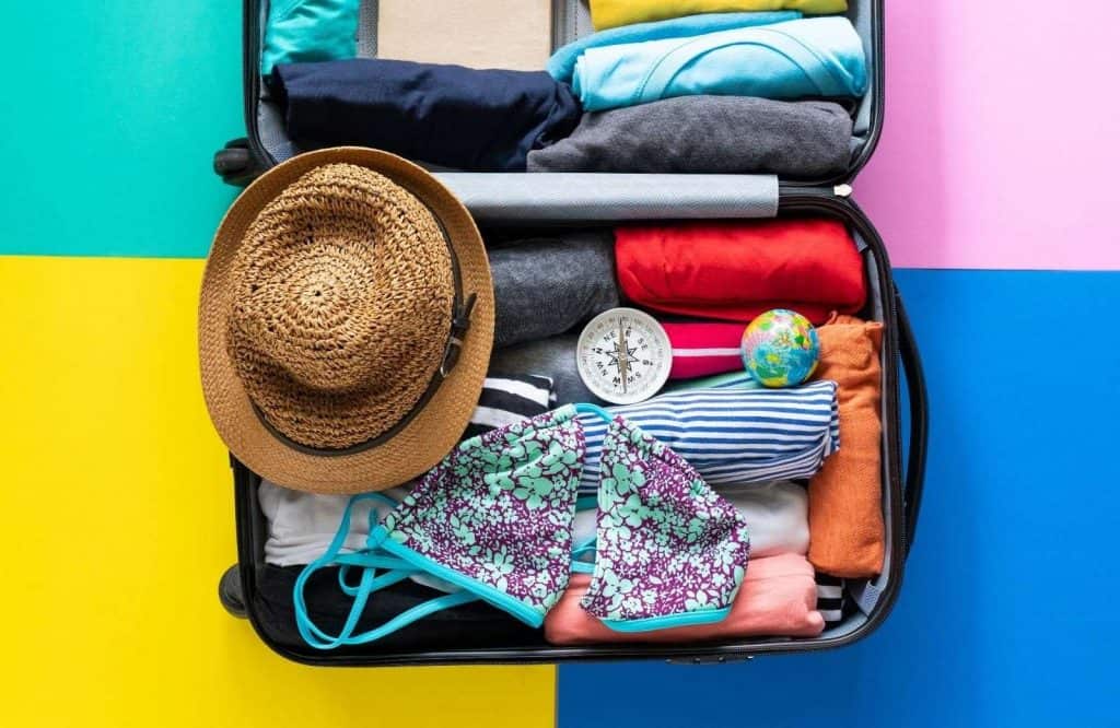 A suitcase filled with clothes behind a colorful background with a packing list for Tulum.