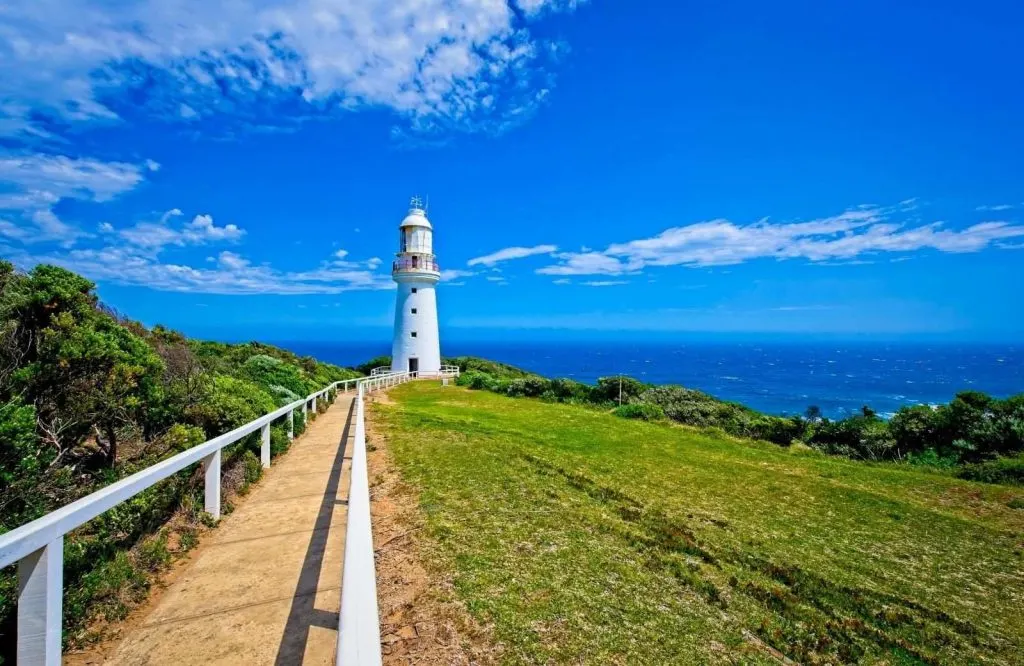 A walking path perched above the shoreline with a white lighthouse at the end, Cape Otway Lighthouse, which is one of many awesome Great Ocean Road stops.