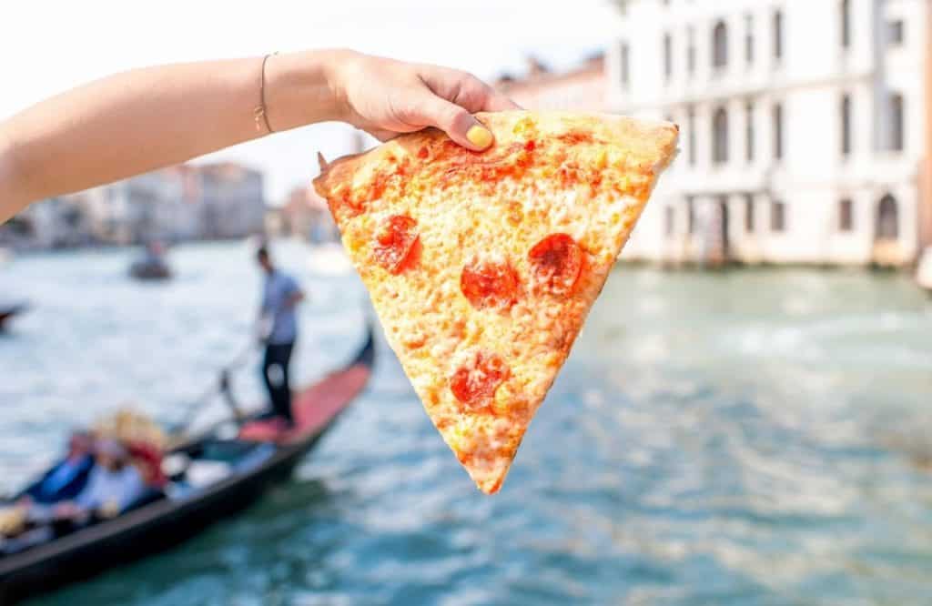 A slice of pizza and eating a cheap lunch to save money is one of the best things to know before visiting Venice.