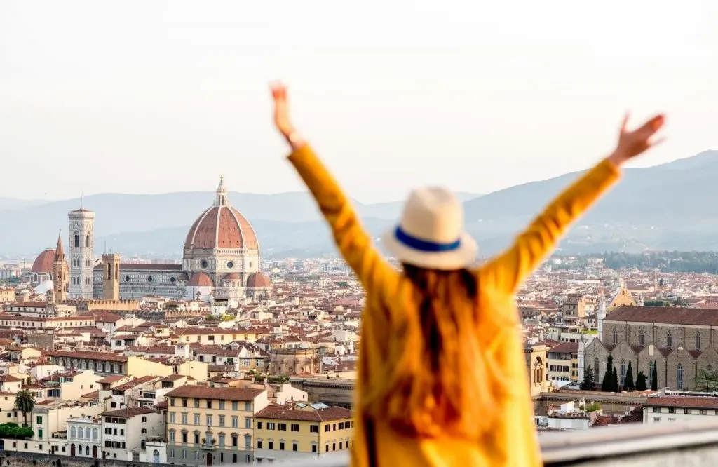 A woman wearing a yellow cardigan with her hands up on Florence Italy for solo travel quotes.