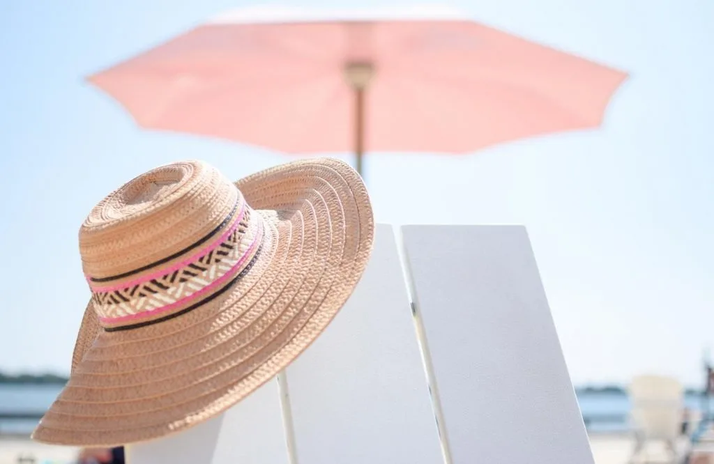 A straw sunhat under a pink umbrella on the beach for a packing list for Tulum Mexico.
