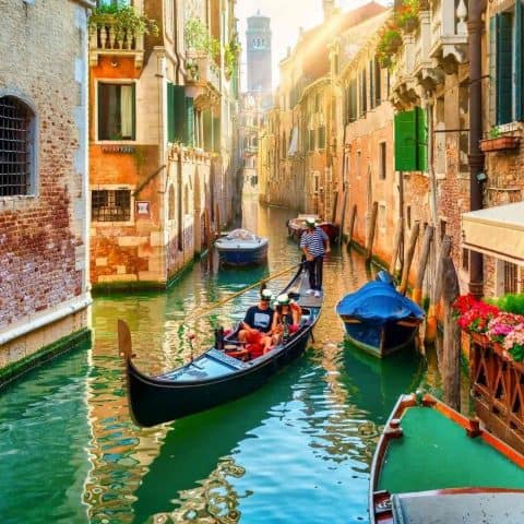 A canal with a gondola with a couple in it for the best things to know before visiting Venice.