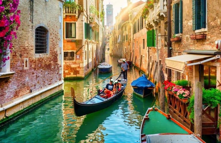 A canal with a gondola with a couple in it for the best things to know before visiting Venice.