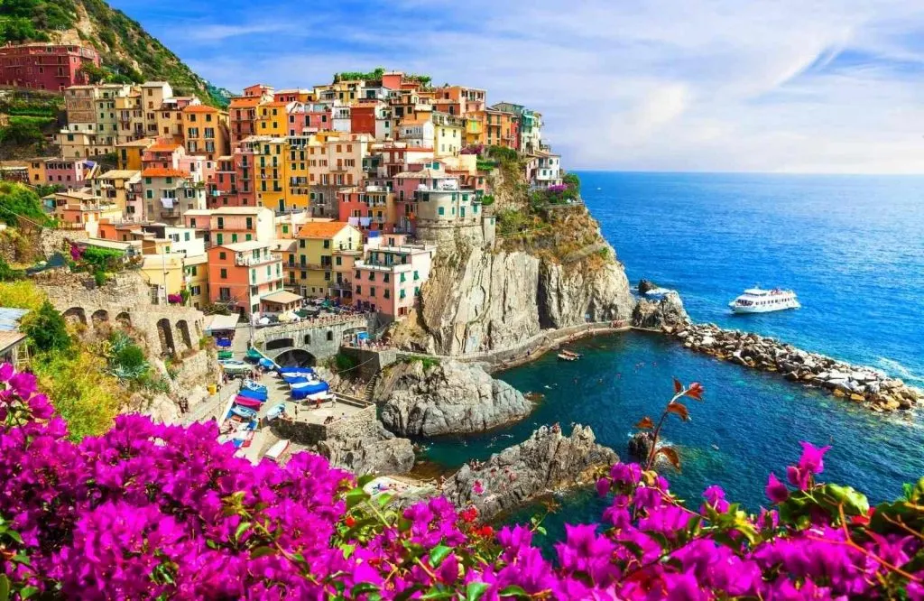 Colorful houses on the coastline with purple flowers which is Cinque Terre, what is Italy known for.