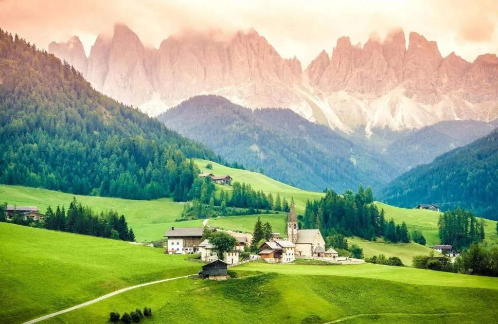 Rolling green hills with houses and the Dolomites behind them, with what is Italy known for.