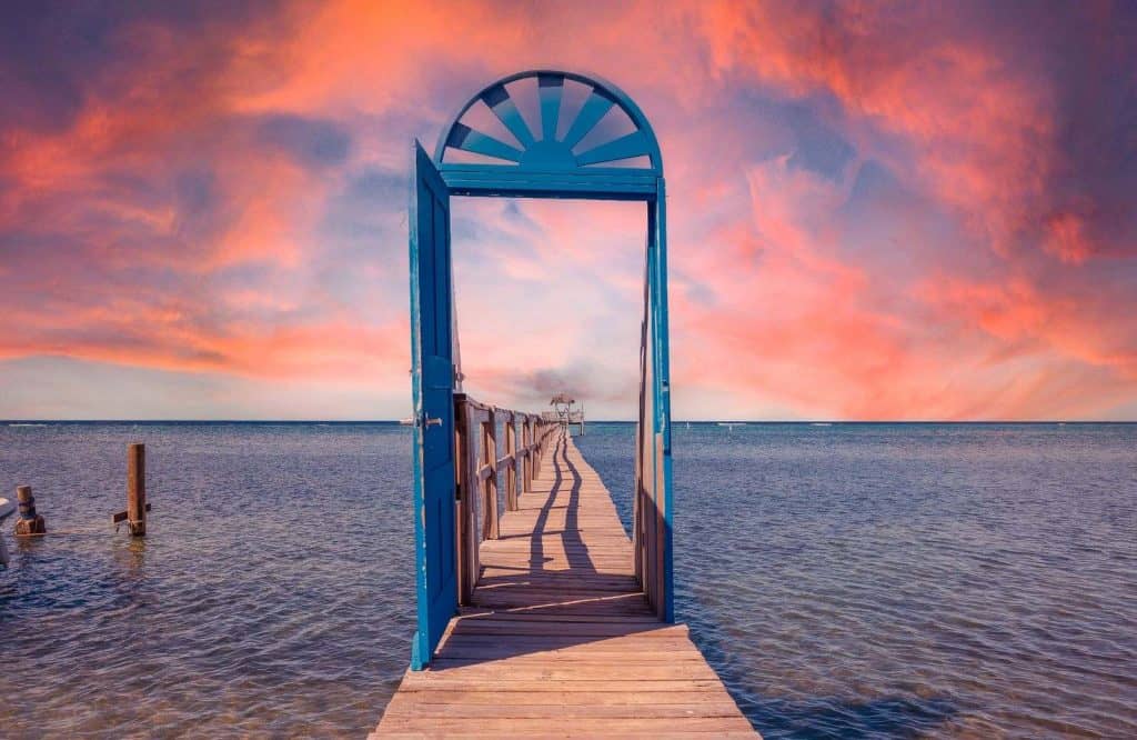 A cotton candy sunset with a blue door perched on a boardwalk for one day in Roatan.