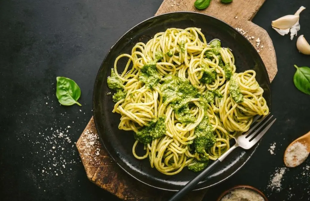 A black plate filled with pesto and noodles which is showing what is Italy famous for.