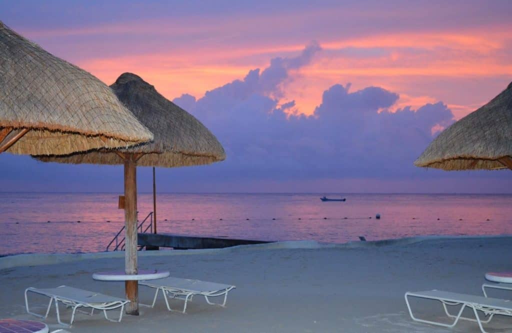 Sunset with pink and purple skies with beach umbrellas for is Cozumel safe.