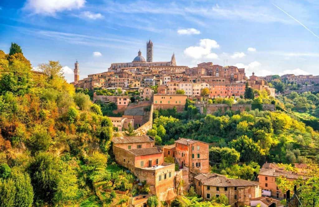 Green trees and bushes with orange roofed buildings in Tuscany, what is Italy known for.