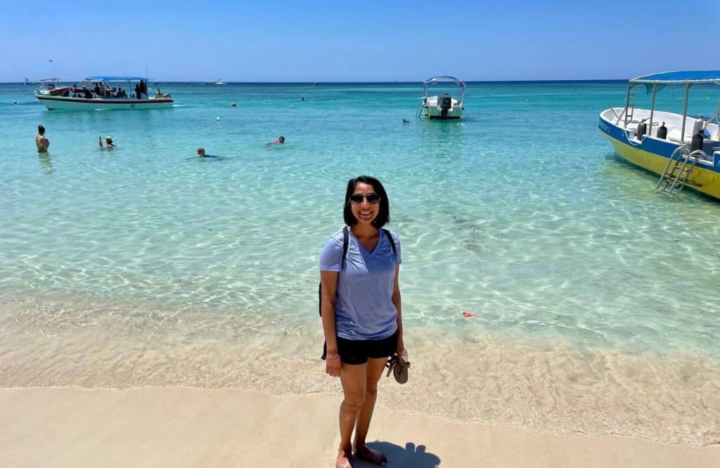A woman (me) standing on the beach with crystal clear waters behind her on her one day in Roatan trip.