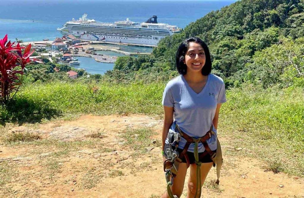 A woman (me) with ziplining gear attached to her standing on a cliffside with a view of a cruise ship and the ocean for one day in Roatan.
