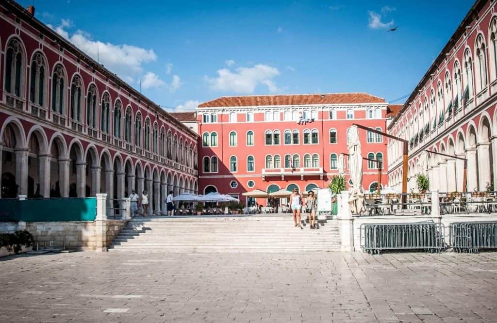 A town square with a light red building which is Republic Square in Split.