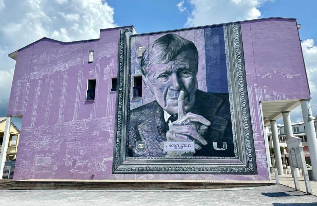 A purple mural on the side of a building with a painting of Vincent Scully's face as a tribute to his legacy.