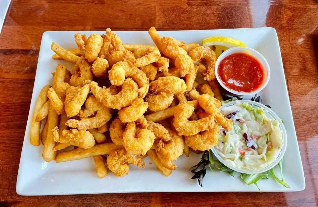A plate of fried shrimp with fries and coleslaw.