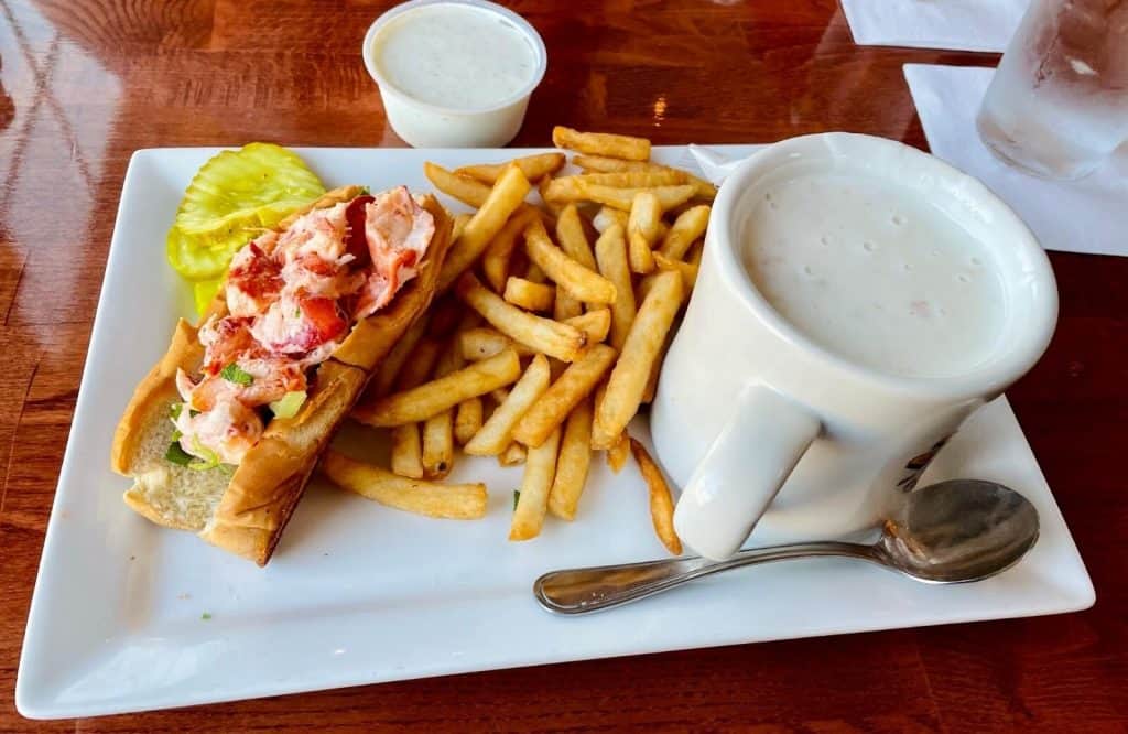 A plate with a lobster roll, fries, and a mug of clam chowder.