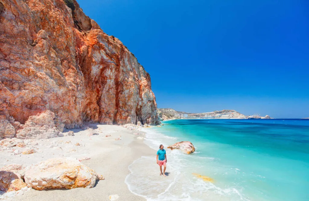 Man walking along the beach in Milos with ornate rock formations on the sand.