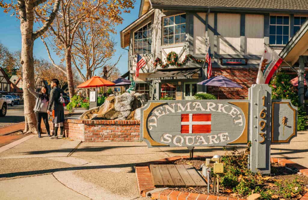 A quaint street in Solvang with a wooden sign that says "Denmarket Square" with a restaurant behind it.