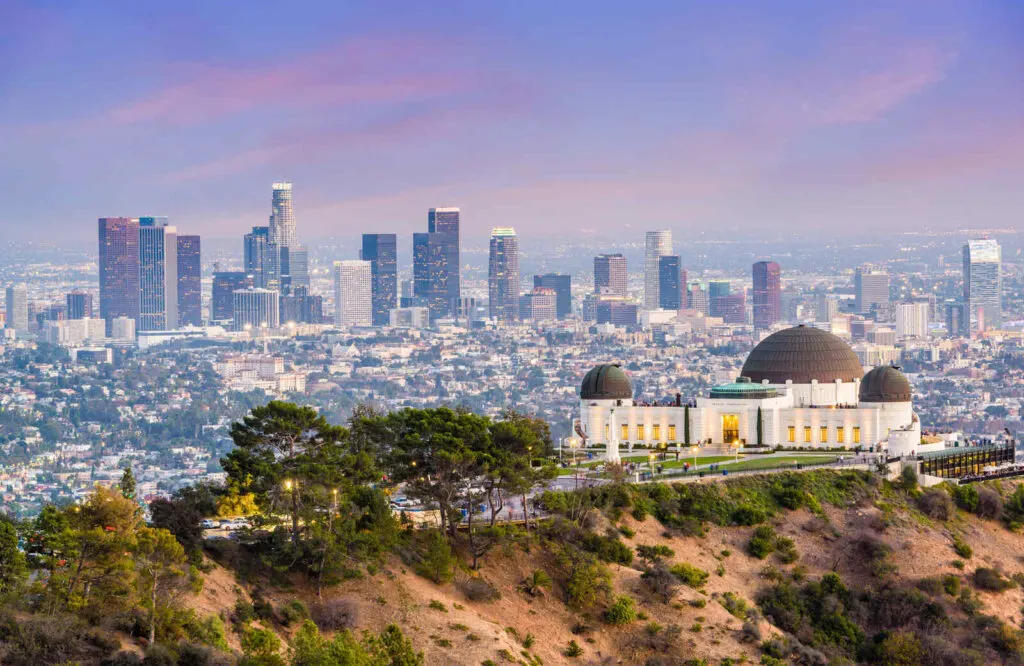 Griffith Observatory in front of tall buildings at dusk during 2 days in Los Angeles.