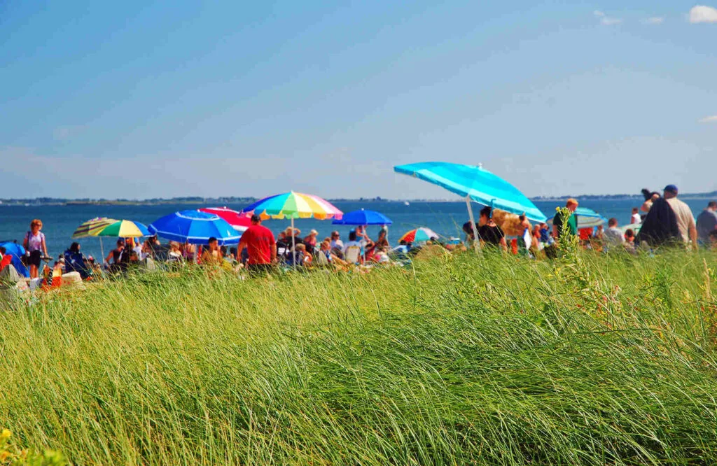Beachgoers with colorful umbrellas behind sand dunes enjoying Old Orchard Beach.