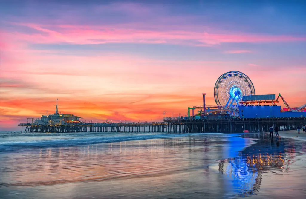 A ferris wheel and a pier on the beach at sunset which is the Santa Monica Pier.