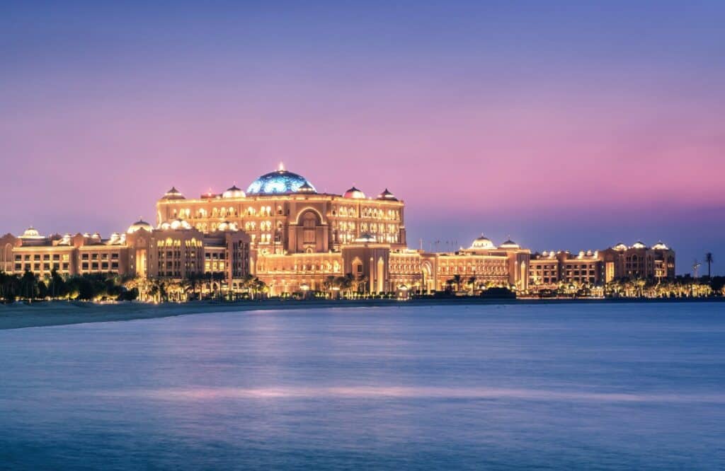 Sunset view of the Emirates Palace hotel in Abu Dhabi along the ocean.