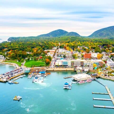 Aerial view of a town on the harbor with buildings and mountains in the background which shows things to do in Bar Harbor Maine.