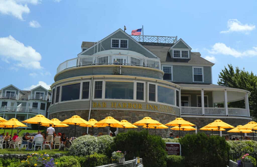 The exterior of the Bar Harbor Inn with yellow umbrellas and tables outside.