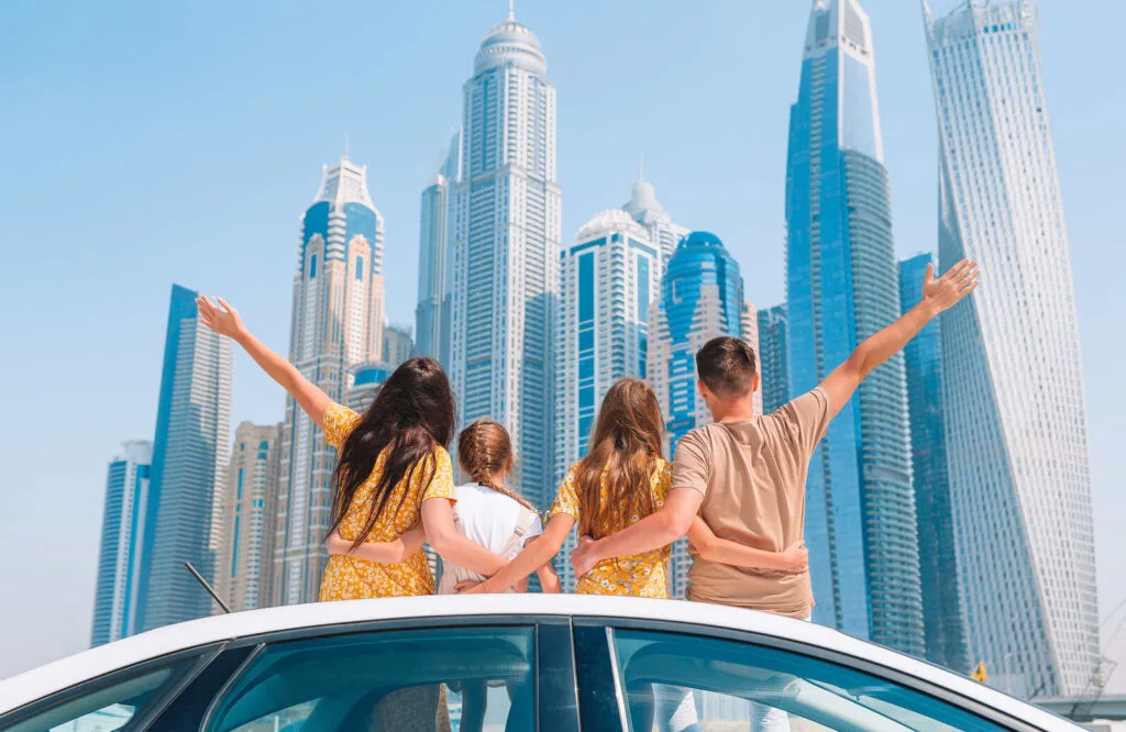 A family of four people in the sunroof of a car overlooking the Dubai skyline.
