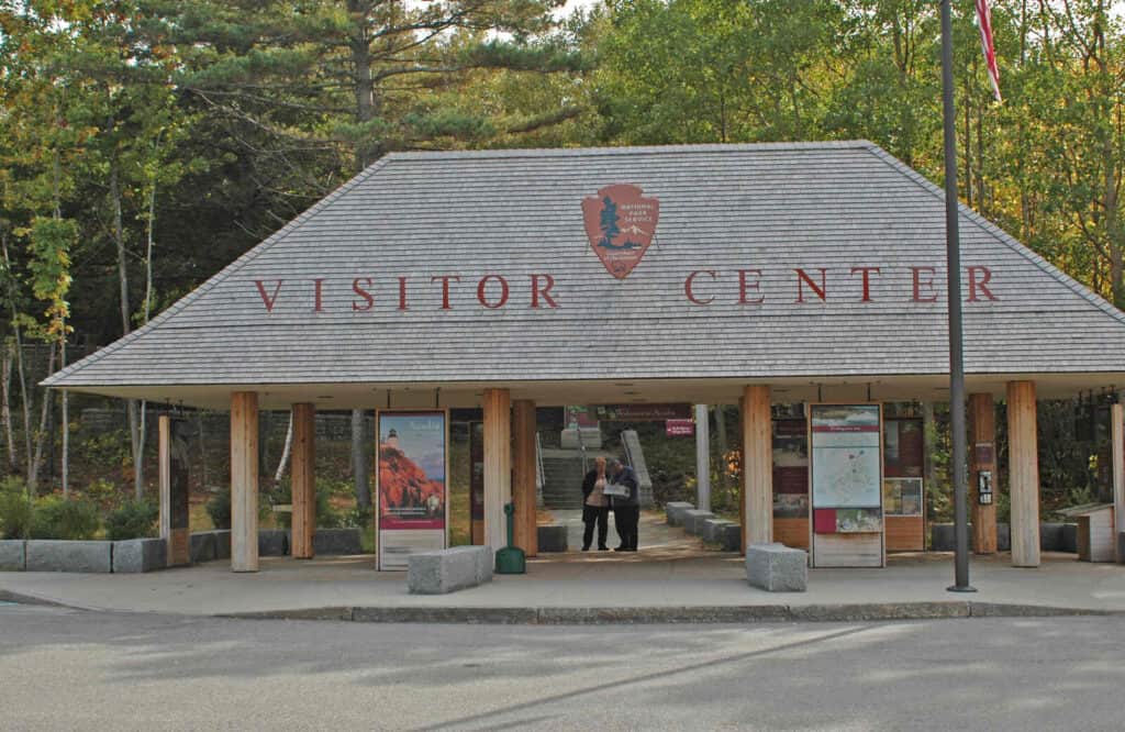 The exterior of Hulls Cove Visitor Center in Acadia National Park with a brown roof with a sign that says "visitor center."