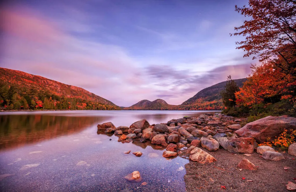 Jordan Pond in Acadia National Park with two mountain peaks in the background and large pebbles scattered around the lake.