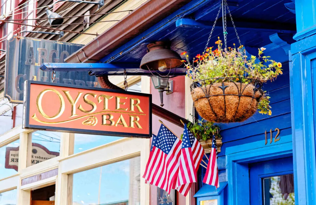 Blue building with sign that says "oyster bar" with a few American flags, which is one of several things to do in Bar Harbor.