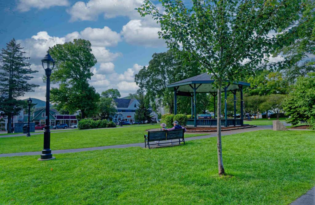 A park with a bench and gazebo with bright green grass which is Village Green in Bar Harbor.