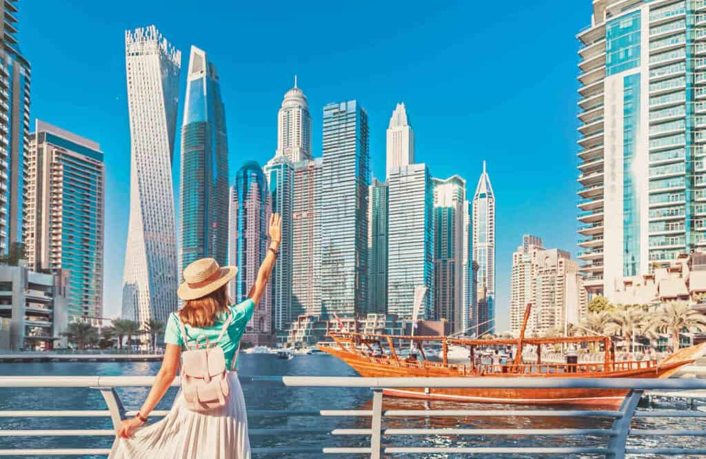A woman tourist wearing a blue shirt and a cream skirt posing at the Dubai Marina.