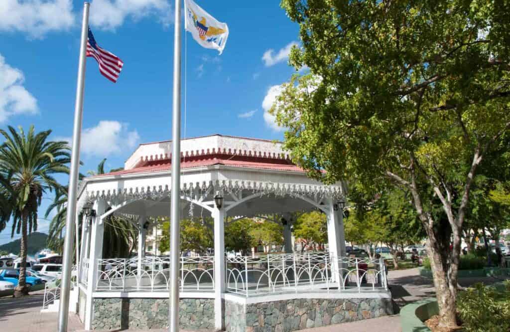 A white gazebo with a red roof and two flags surrounded by trees at Emancipation Garden.
