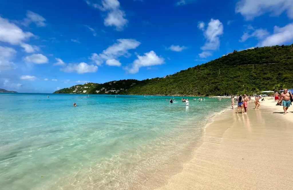 Golden white sandy beach with clear blue waters and a lush mountain behind it, which is Magens Bay Beach and one of the best things to do on Saint Thomas.