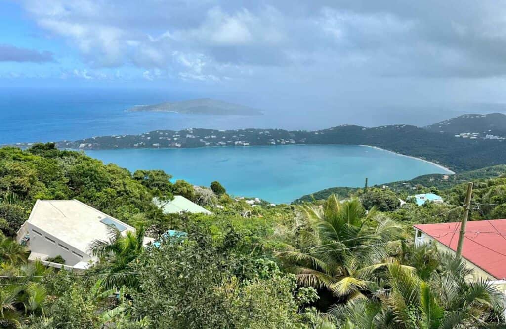 Panoramic view of Magens Bay from The Mountain Top with cloudy skies and clear blue water with lush trees.