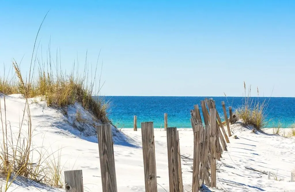 A sand dune and wood fencing along Princess Beach leading to beautiful blue waters, one of many beaches in Destin Florida.