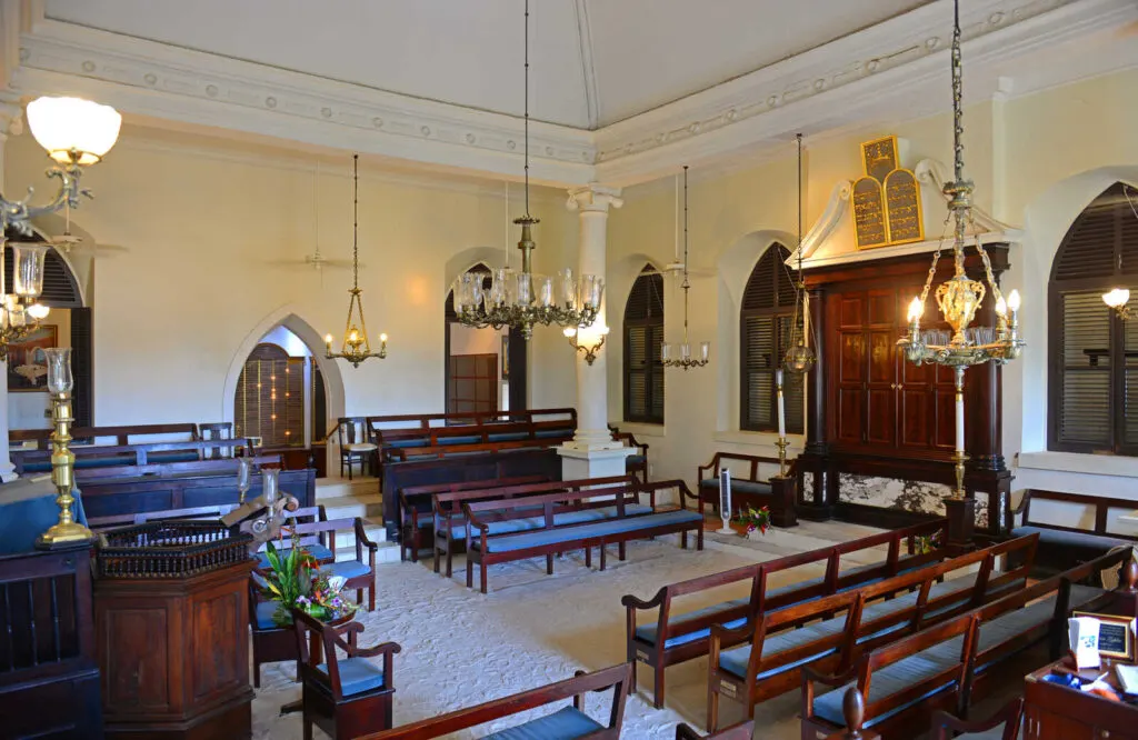 The interior of St. Thomas Synagogue with wooden pews and ornate chandeliers.