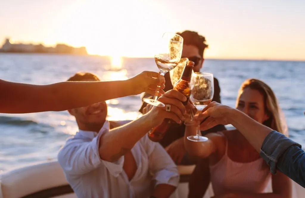A group of friends on a boat with the sunset behind them while cheering each other with their drinks.