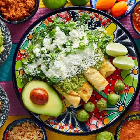 A plateful of enchiladas topped with salsa verde surrounded by sides which you can try on some Cancun food tours.