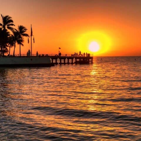 A sunset with bright orange skies behind a pier on the water, which is perfect for sunset cruises in Key West.