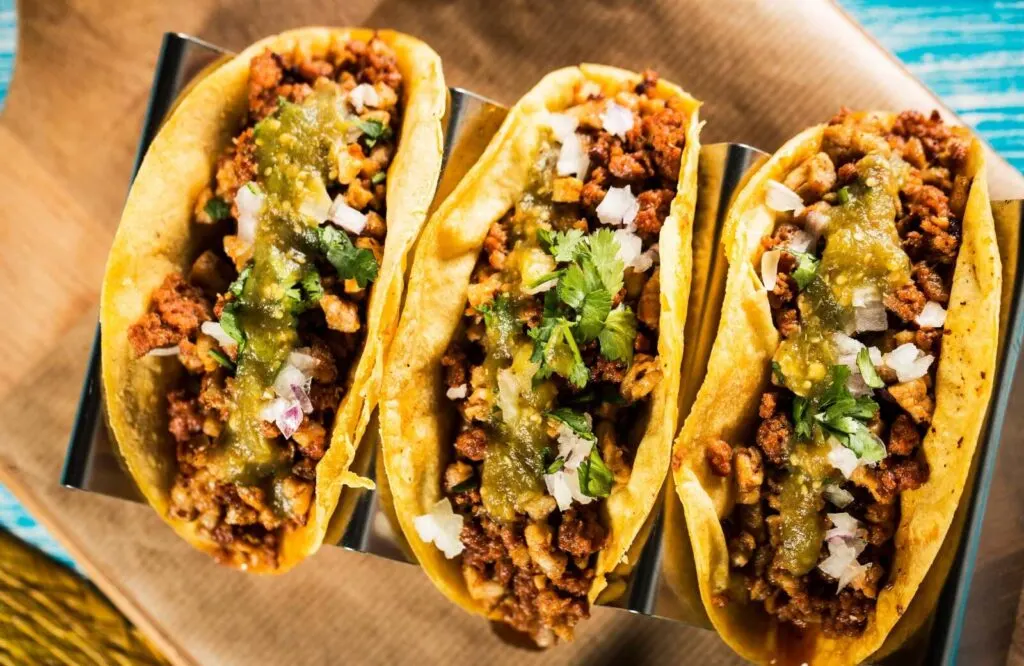 Three tacos filled with meat and topped with salsa verde, onions, and cilantro which you can sample on several Cancun food tours.